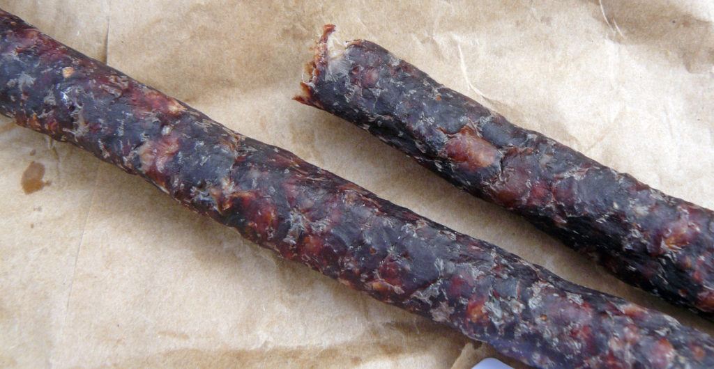 An image of two cured sticks of droëwors sausage on a brown paper bag